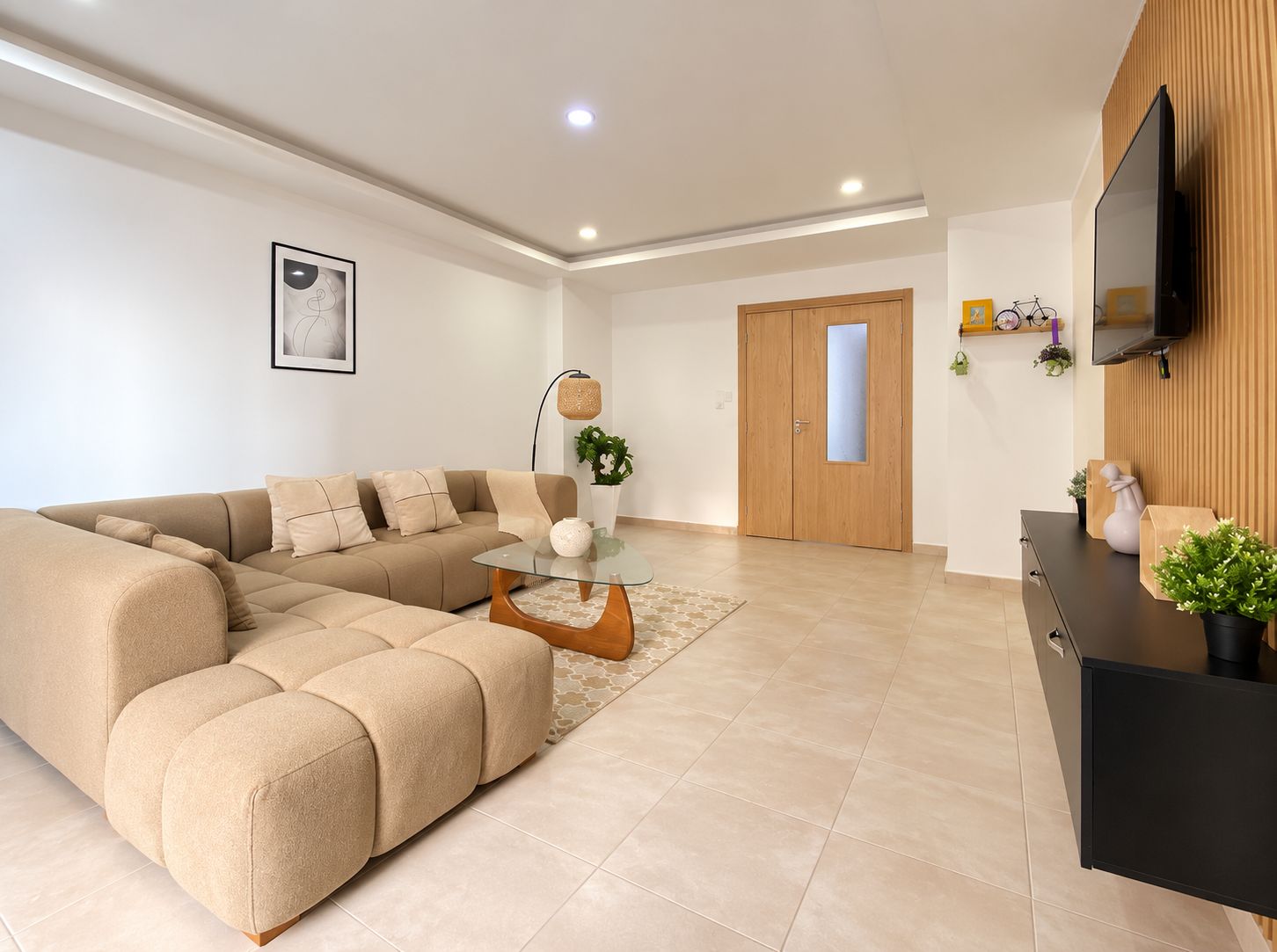 A modern living room with a sectional sofa, a glass coffee table, and a wooden door in the background.