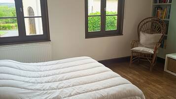 Une chambre à coucher avec un lit, deux fenêtres, une chaise et une bibliothèque.