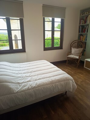 Une chambre à coucher avec un lit, deux fenêtres, une chaise et une bibliothèque.