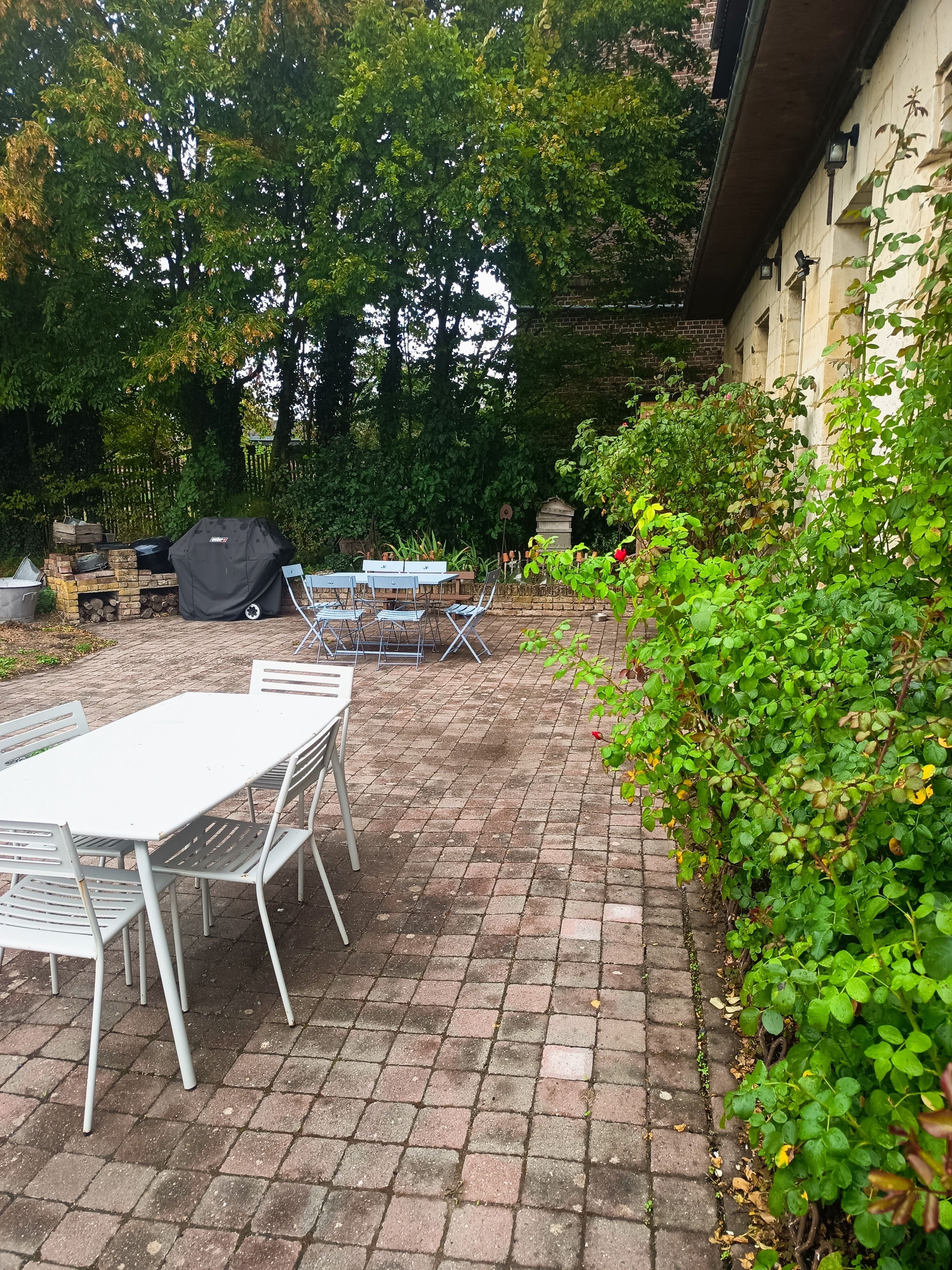Une terrasse extérieure avec un sol en briques, un barbecue abrité et une table avec des chaises.
