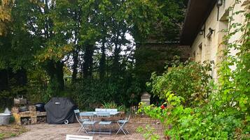 Une terrasse extérieure avec un sol en briques, un barbecue abrité et une table avec des chaises.