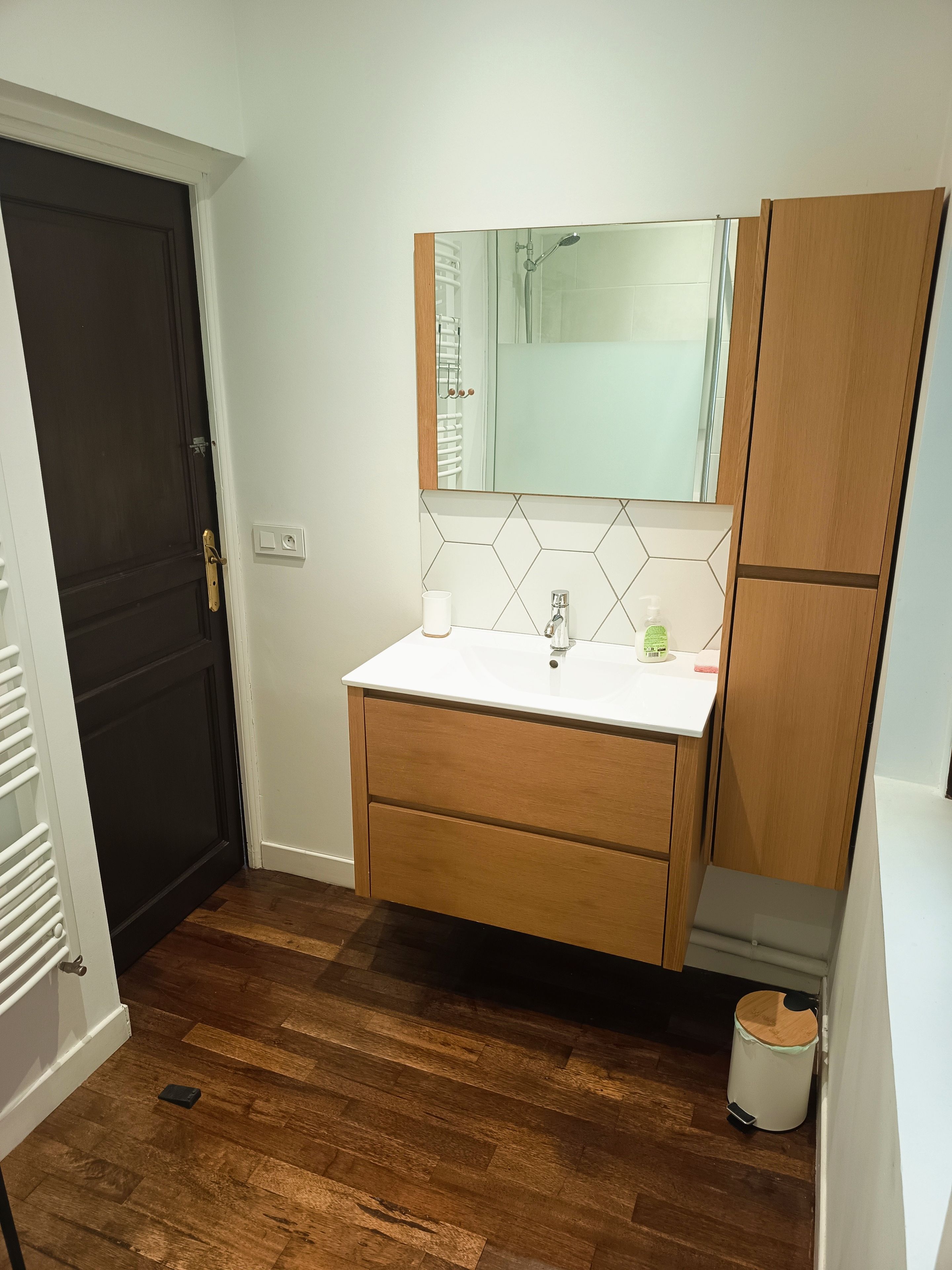 Une salle de bain avec un lavabo blanc, des meubles en bois, un miroir et un espace douche.