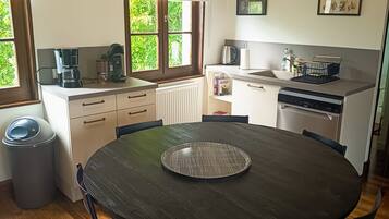 Een keuken met een ronde tafel, stoelen, een koffiezetapparaat en een raam met uitzicht op groen.