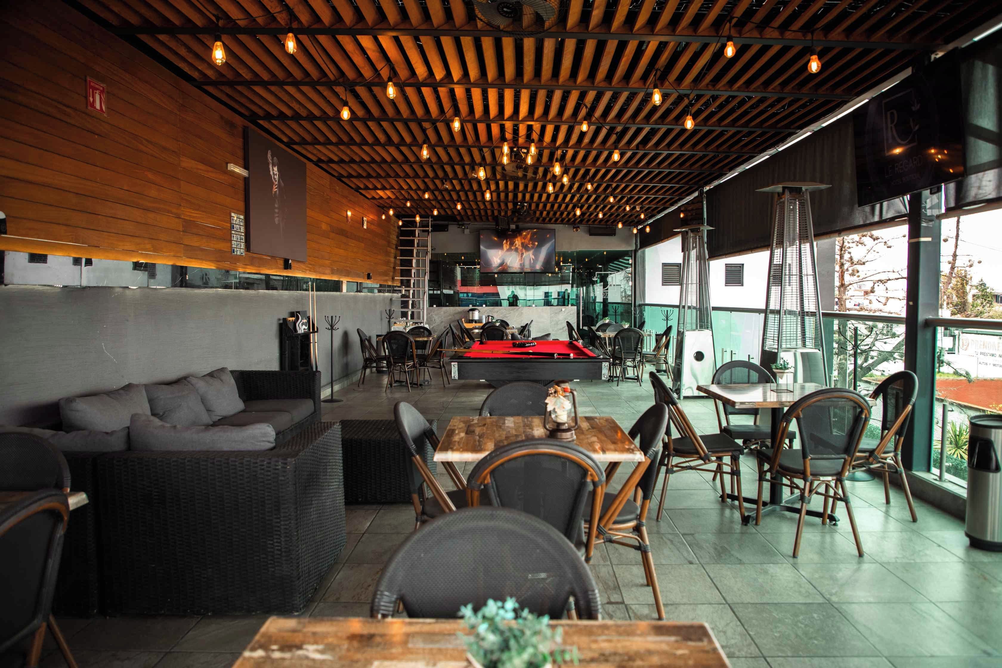 Un comedor interior con vigas de madera en el techo, mesas, sillas y una mesa de billar.