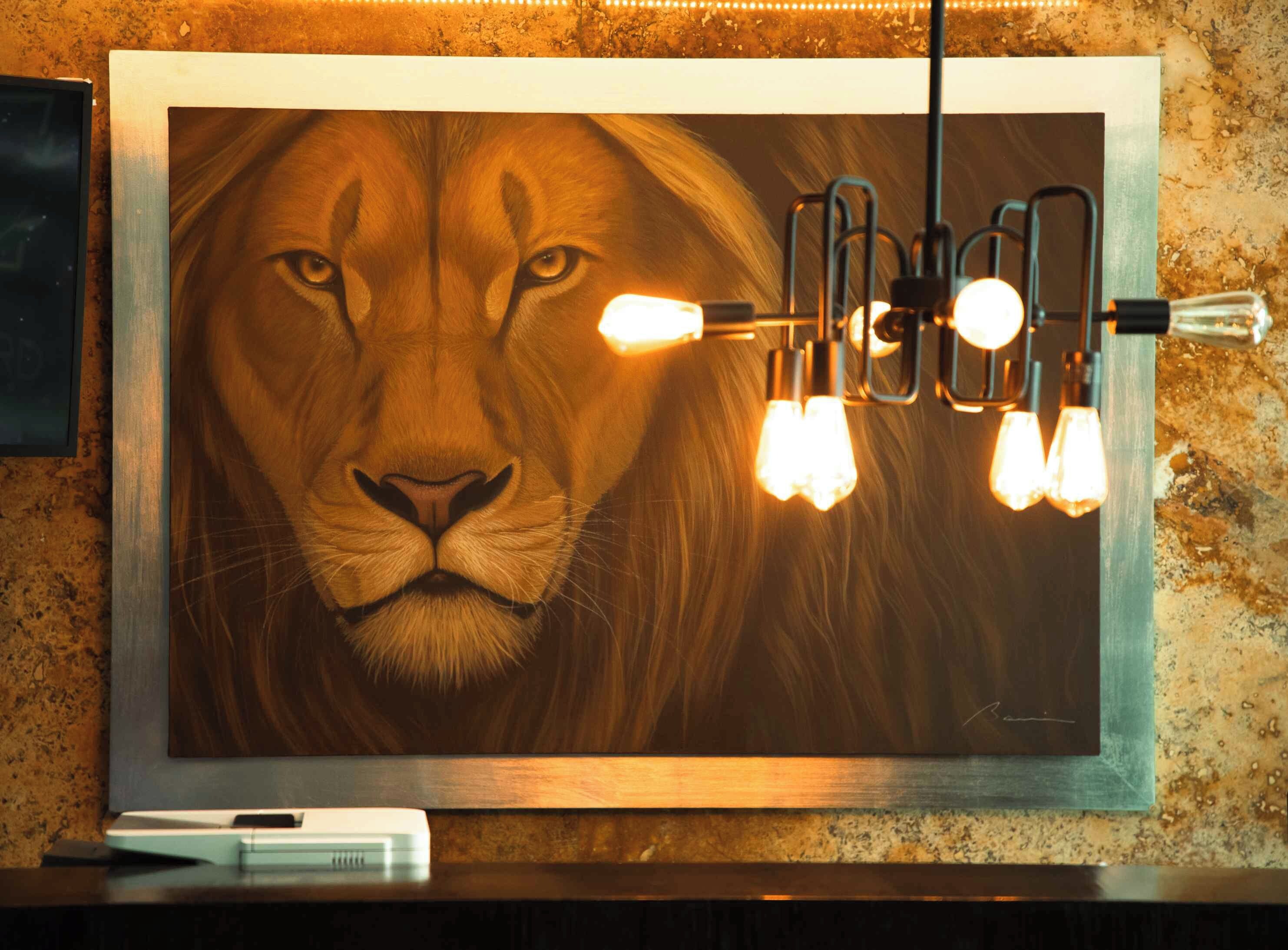 A framed artwork of a lion's face with a light fixture above it.