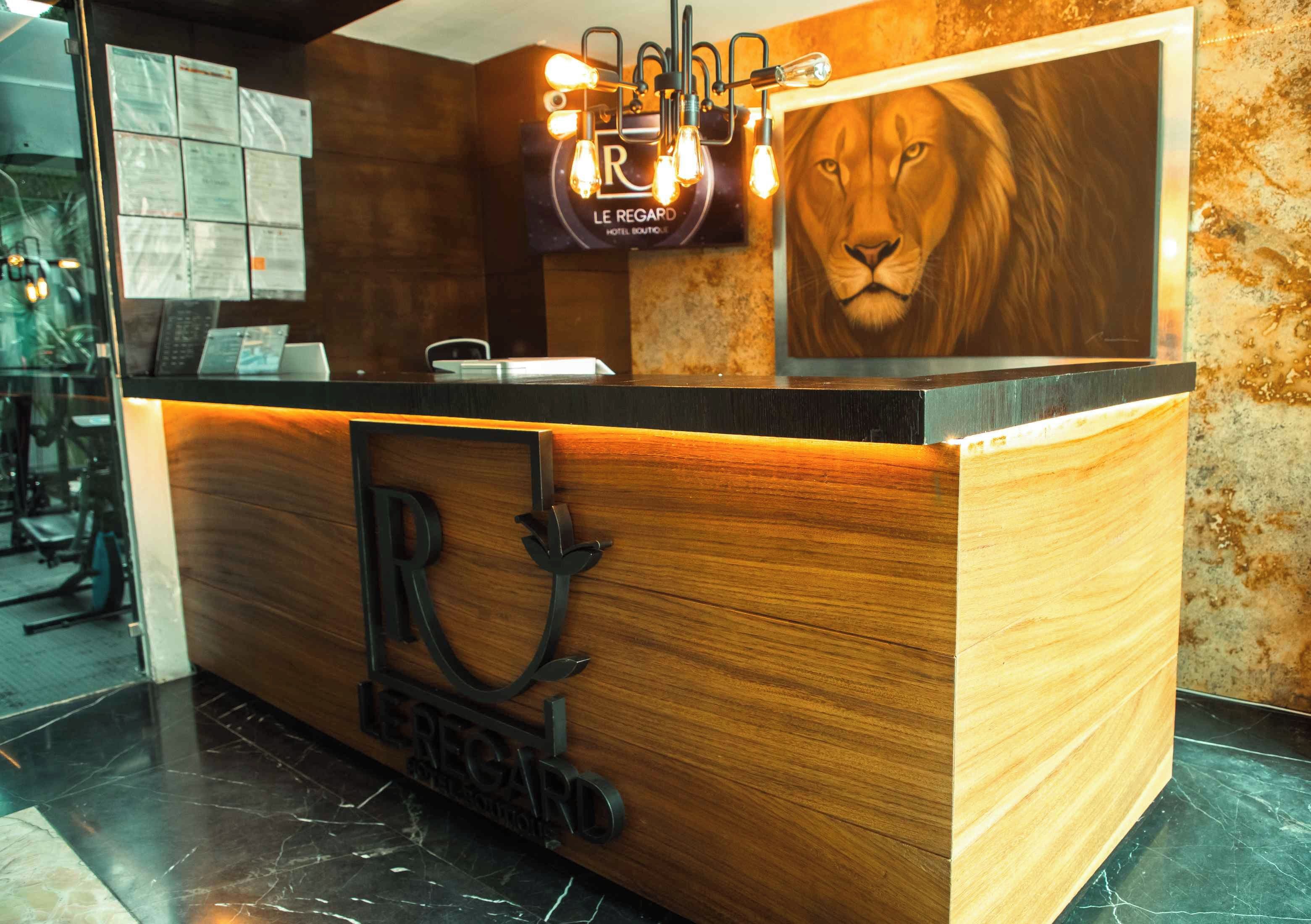 A reception desk with a wooden finish, a lion mural, and a sign reading 'Le Regard Hotel Boutique.'
