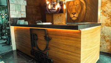 Un comptoir d’accueil avec un revêtement en bois, une fresque représentant un lion et une enseigne indiquant « Le Regard Hotel Boutique ».