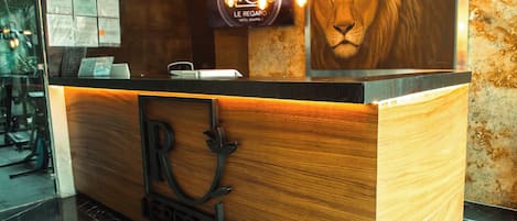 A reception desk with a wooden finish, a lion mural, and a sign reading 'Le Regard Hotel Boutique.'