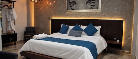 Quarto de hotel moderno com uma cama grande, cabeceira com iluminação integrada, parede de mármore e uma obra de arte emoldurada sobre a cama.