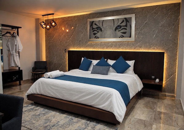 A modern hotel room with a large bed, a headboard with integrated lighting, a marble wall, and a framed artwork above the bed.