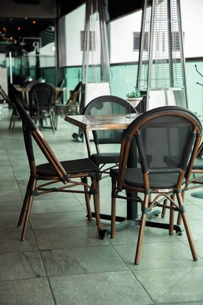 Un interior de restaurante con sillas de mimbre, una mesa y vistas del paisaje urbano a través de amplias ventanas.