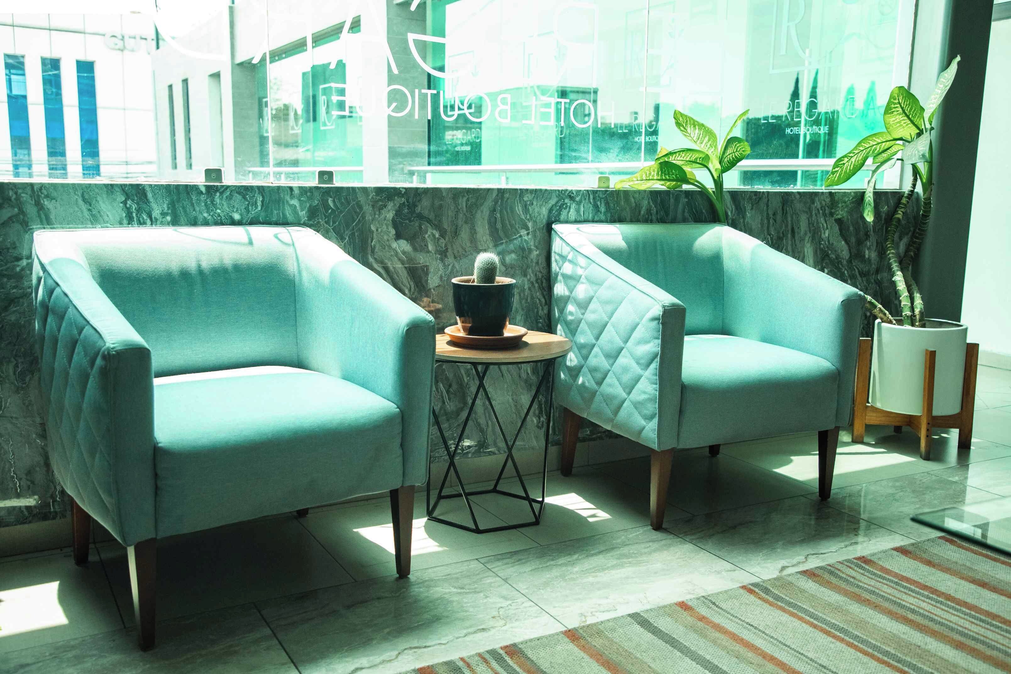 Dos sillones, una mesita con una planta en maceta y una ventana con vista a edificios.