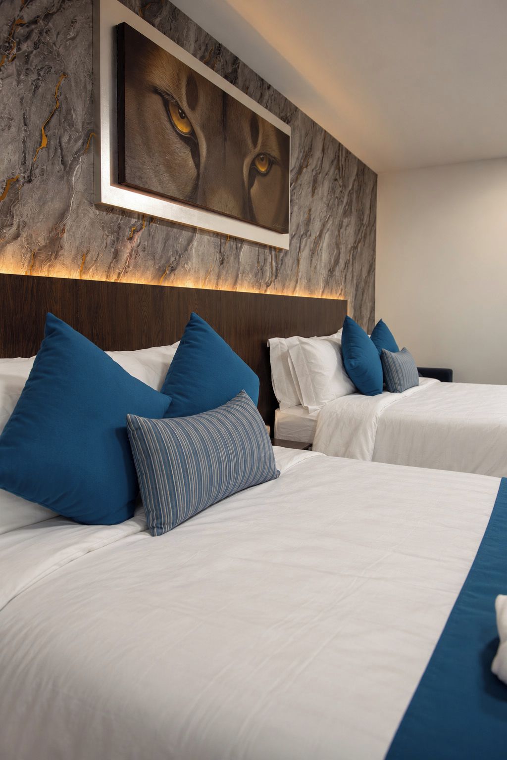 Habitación de hotel con dos camas, cada una con ropa de cama blanca y almohadas azules.