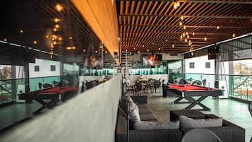 Un espace de loisirs intérieur comprenant des tables de billard, des sièges et un grand écran.