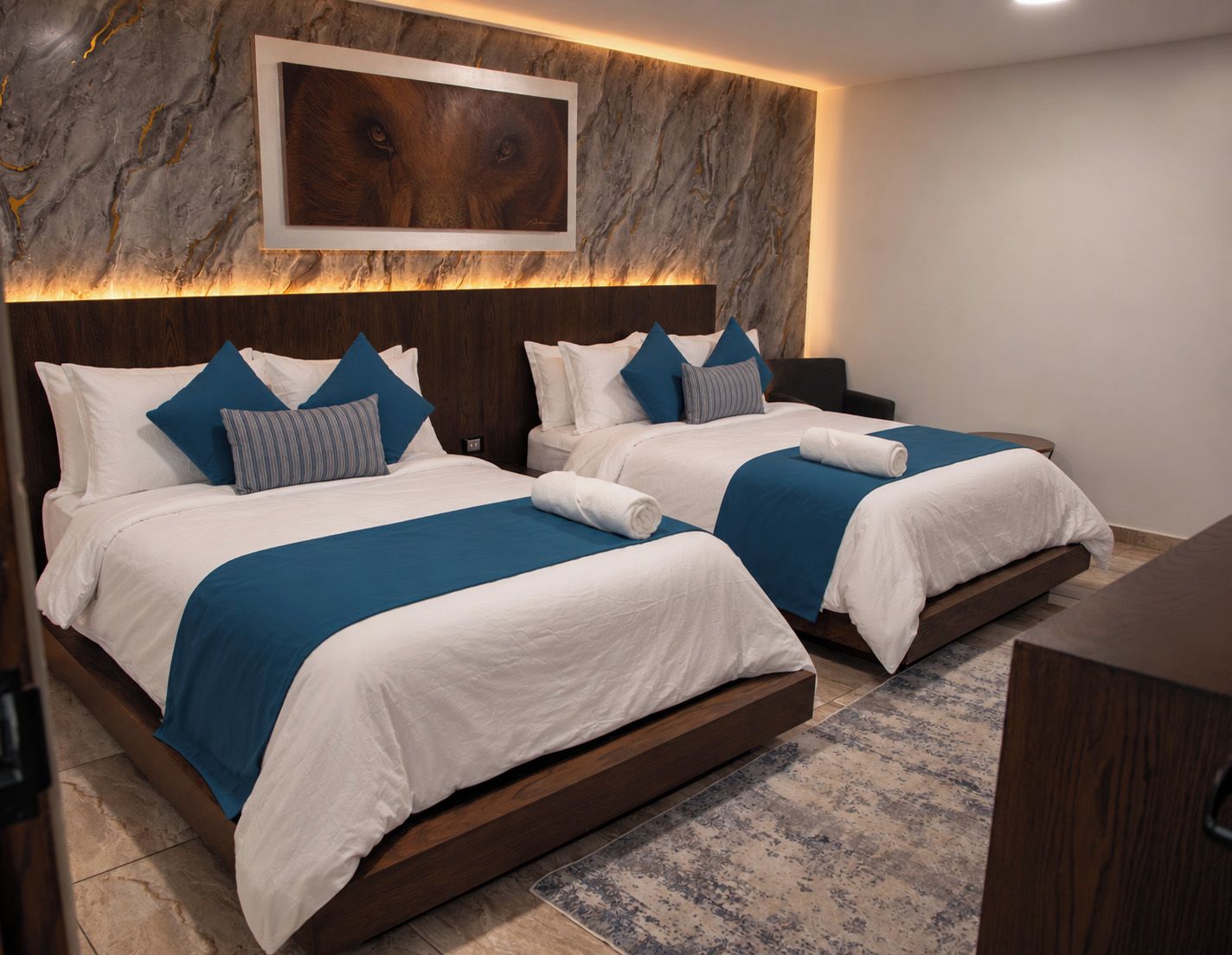 Habitación de hotel con dos camas, una pared de mármol y una obra de arte enmarcada sobre las camas.