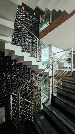 Una escalera moderna con barandillas de vidrio y balaustradas de metal, que conduce a diferentes niveles del edificio.