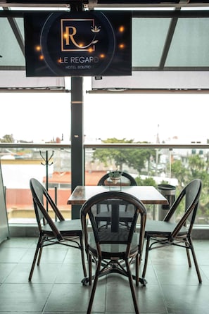 A restaurant with a view, featuring a table and chairs, and a sign above indicating it's 'LE REGARD HOTEL BOUTIQUE'.