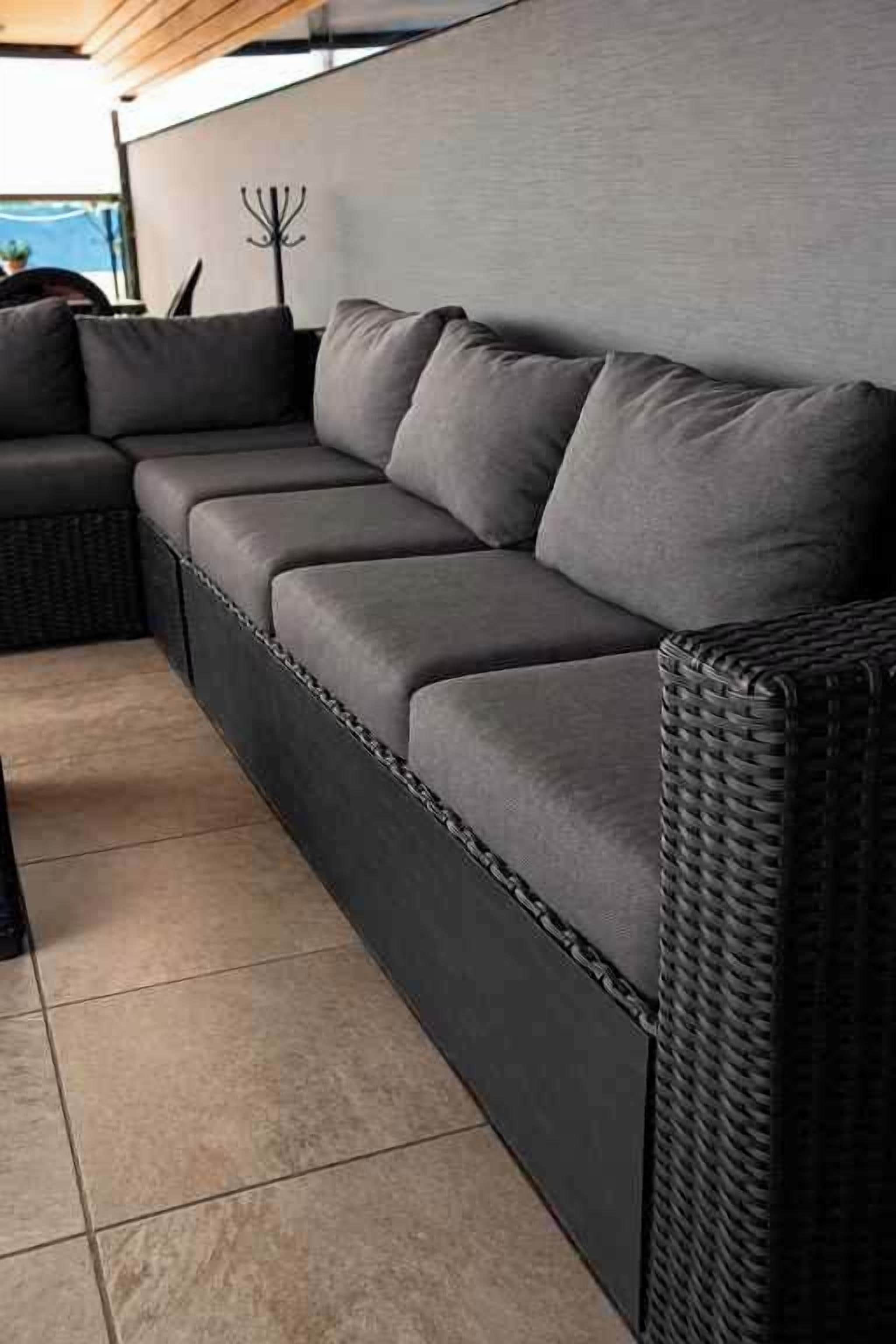 Un sofá modular con tela oscura y estructura trenzada, colocado frente a una pared de tono claro.