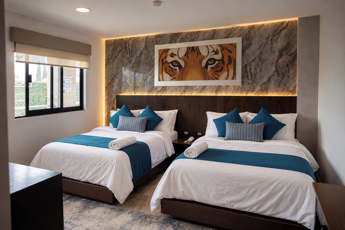 A hotel room with two beds, a marble headboard, a tiger painting, and a window with a view.