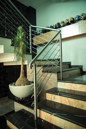 A modern staircase with a metal railing, a potted plant, and a series of decorative masks on the upper landing.
