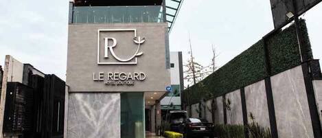 A modern hotel building with a prominent logo and the name 'LE REGARD HOTEL BOUTIQUE'.
