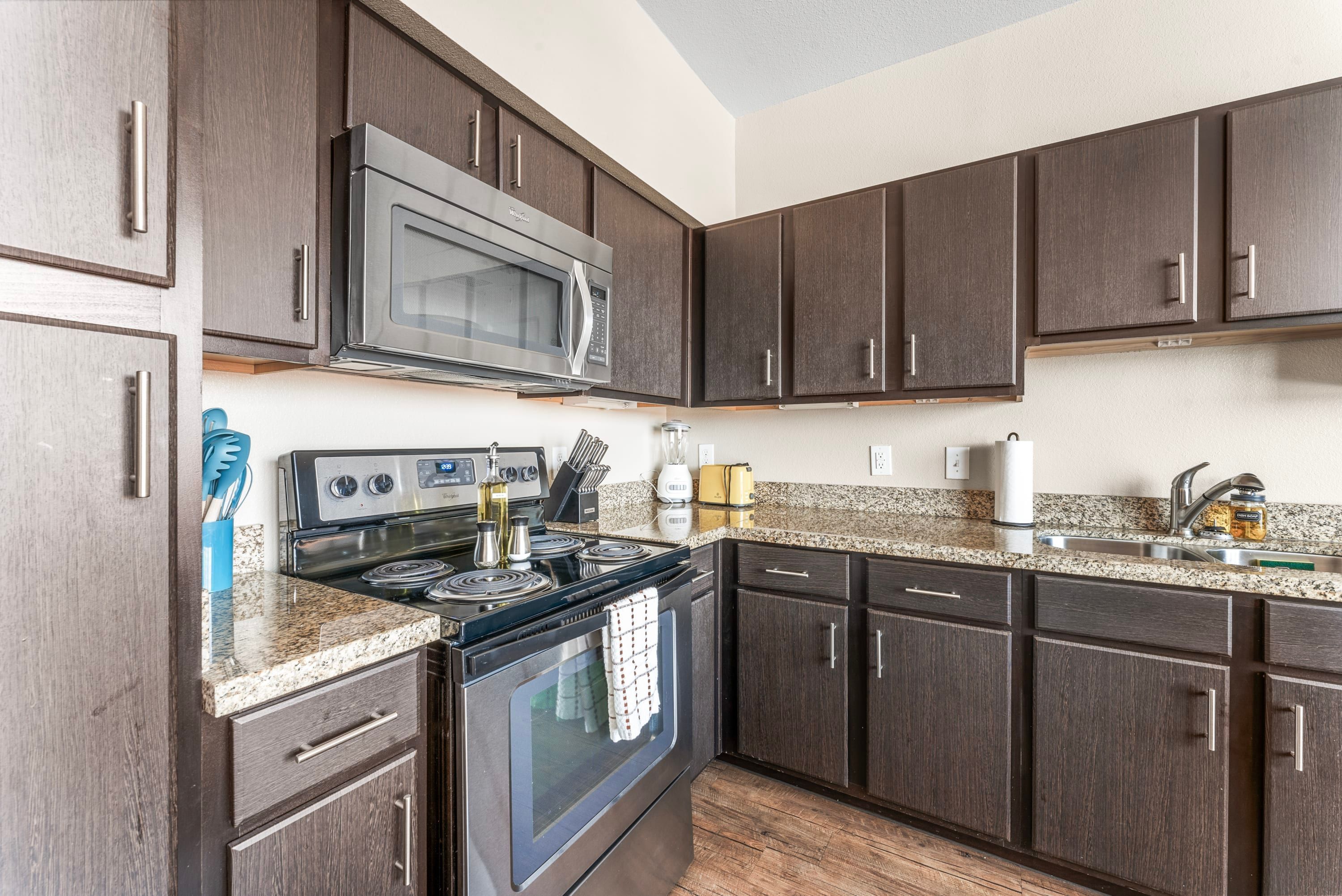 A modern kitchen with dark wood cabinets, stainless steel appliances, and granite countertops.