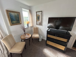 A hotel room with a flat-screen TV, a sofa, a small round table with a vase, and a window with curtains. - kroen ved åen (Skive)