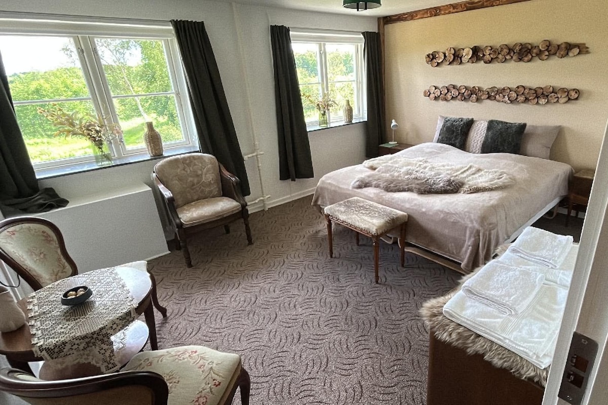 A bedroom with a bed, a chair, a small table, and a window with curtains.