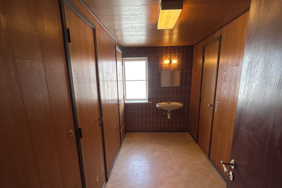 A narrow hallway with wooden doors, a window, and a sink.