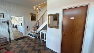 Un vestíbulo de hotel con una escalera, una lámpara de araña, un espejo y una puerta con la leyenda 'Inodoro'.