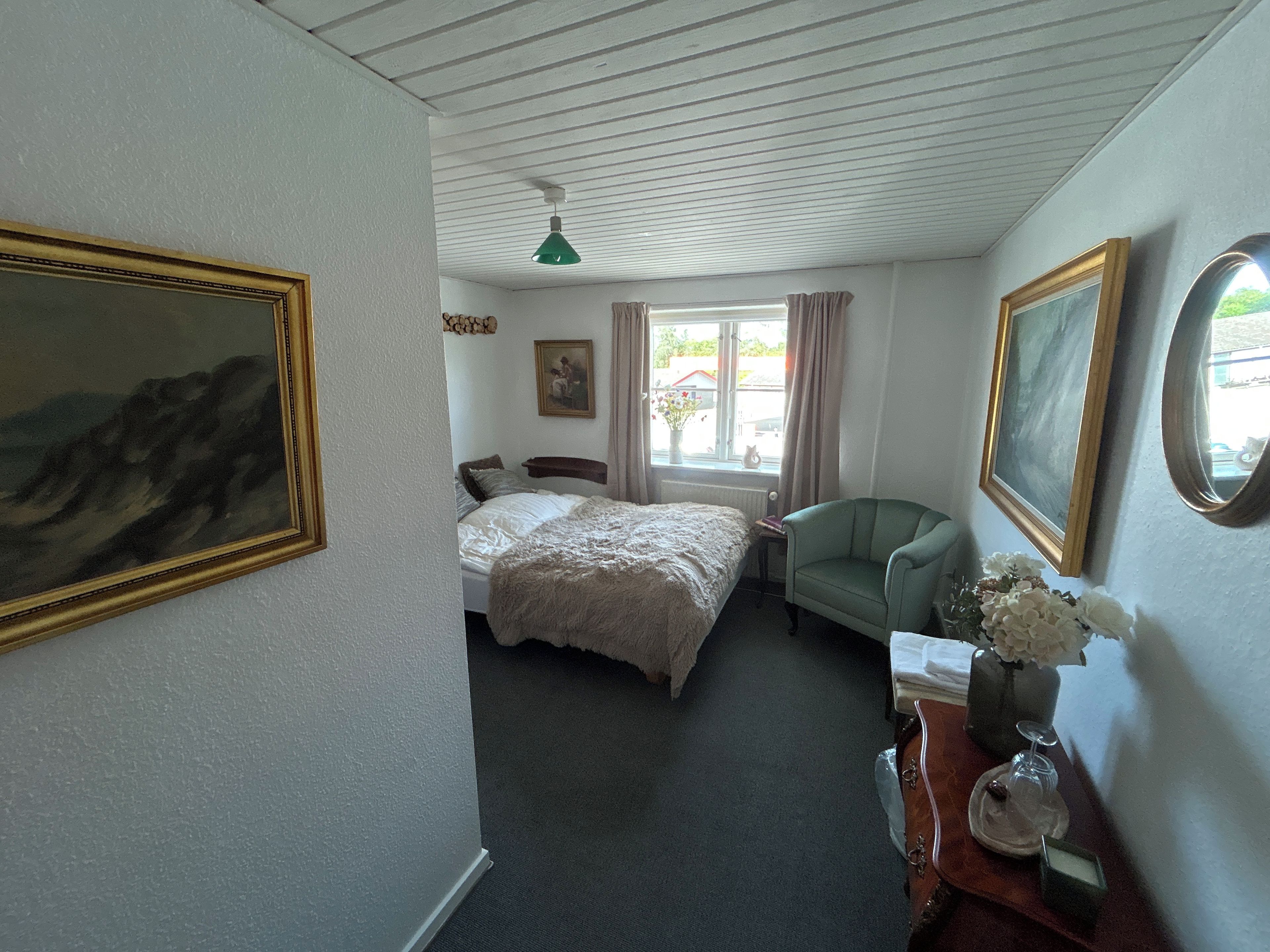 A bedroom with a bed, a chair, a dresser, and a window with curtains.