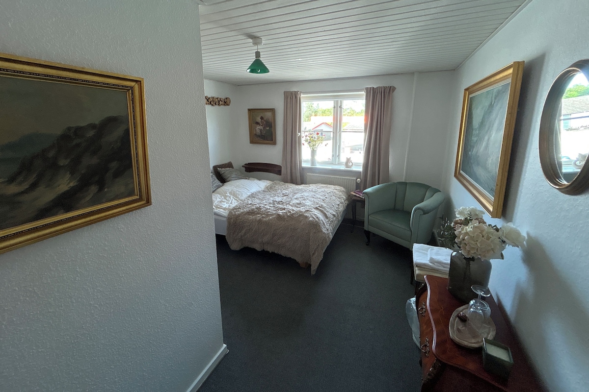 A bedroom with a bed, a chair, a dresser, and a window with curtains.