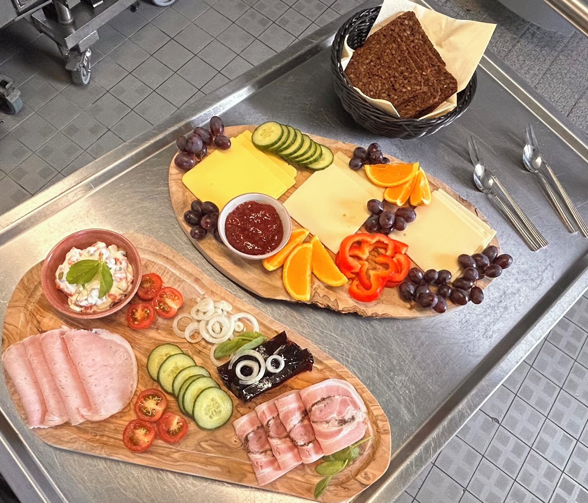 A wooden board with various food items including cheese, grapes, and sliced vegetables.