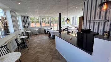 Interior de restaurante con suelo en espiga, mesas blancas y sillas negras.