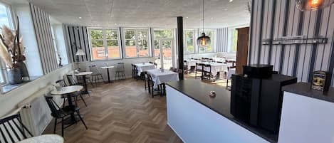A restaurant interior with a herringbone floor, white tables, and black chairs.