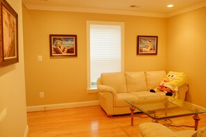 A living room with a beige sofa, a glass coffee table, and two framed paintings on the wall. - 3-bedroom private guesthouse with door parking & water filter (Annandale)
