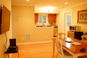 A kitchen with wooden cabinets, a dining table with chairs, a television mounted on the wall, and a microwave. - 3-bedroom private guesthouse with door parking & water filter (Annandale)