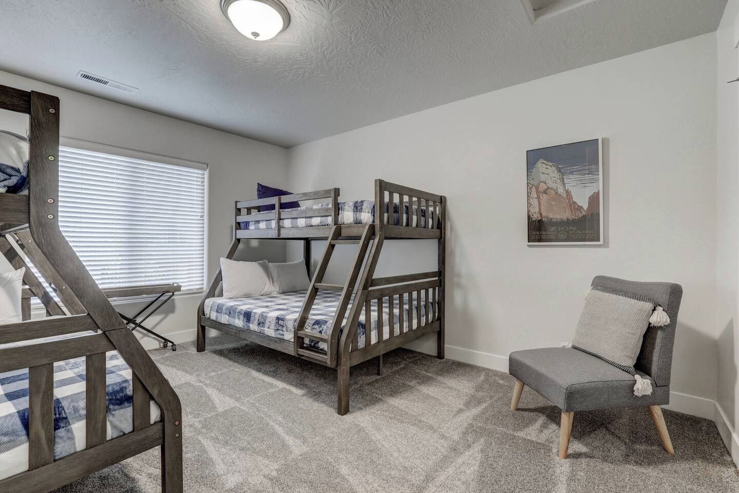 A room with a bunk bed, a chair, and a window with blinds.