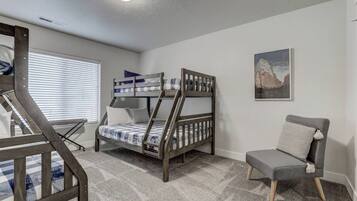 A room with a bunk bed, a chair, and a window with blinds.