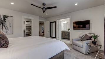 A bedroom with a large bed, a ceiling fan, a TV, and a small side table with a plant.