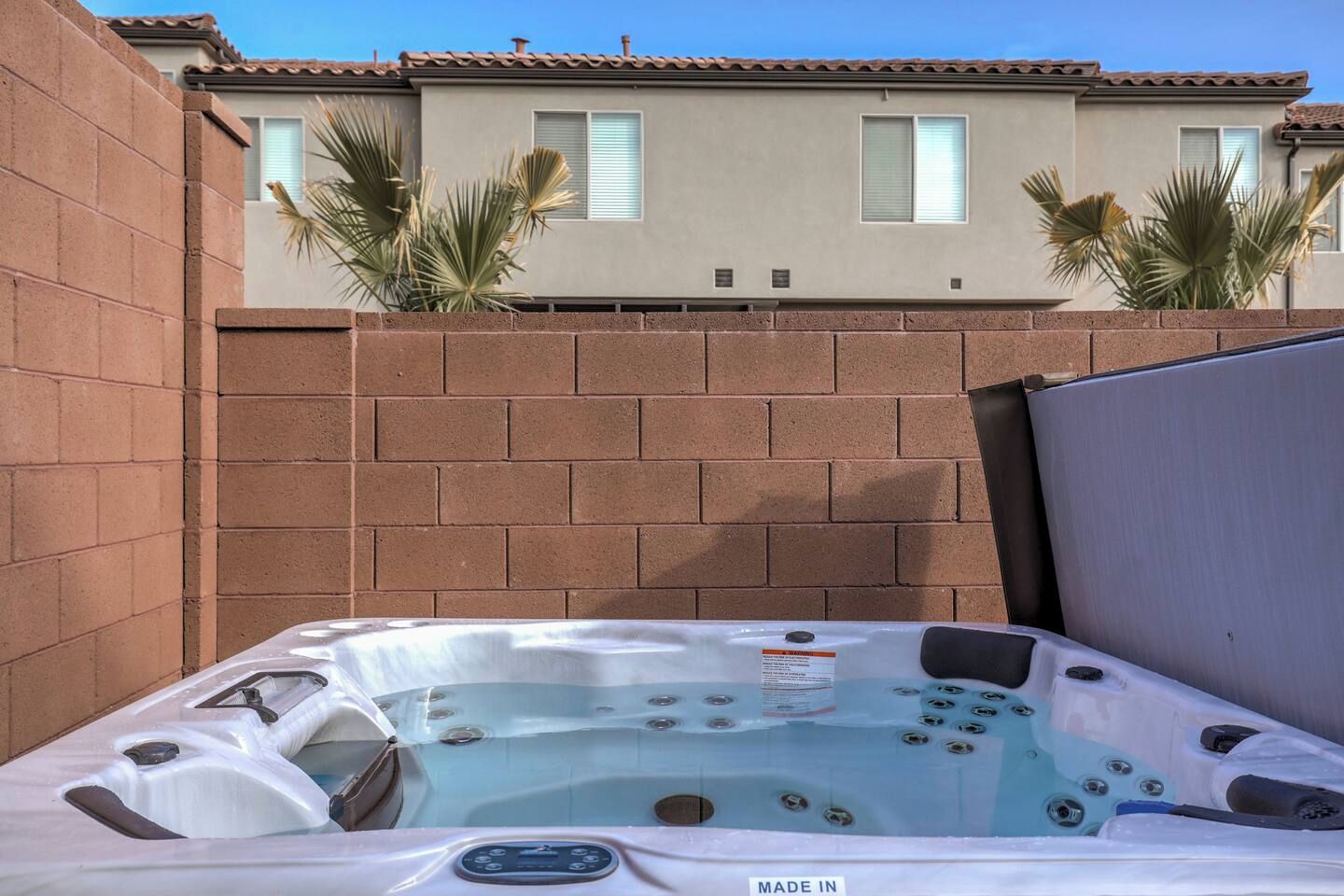 Un jacuzzi con panel de control, frente a un muro de ladrillo y una casa al fondo.