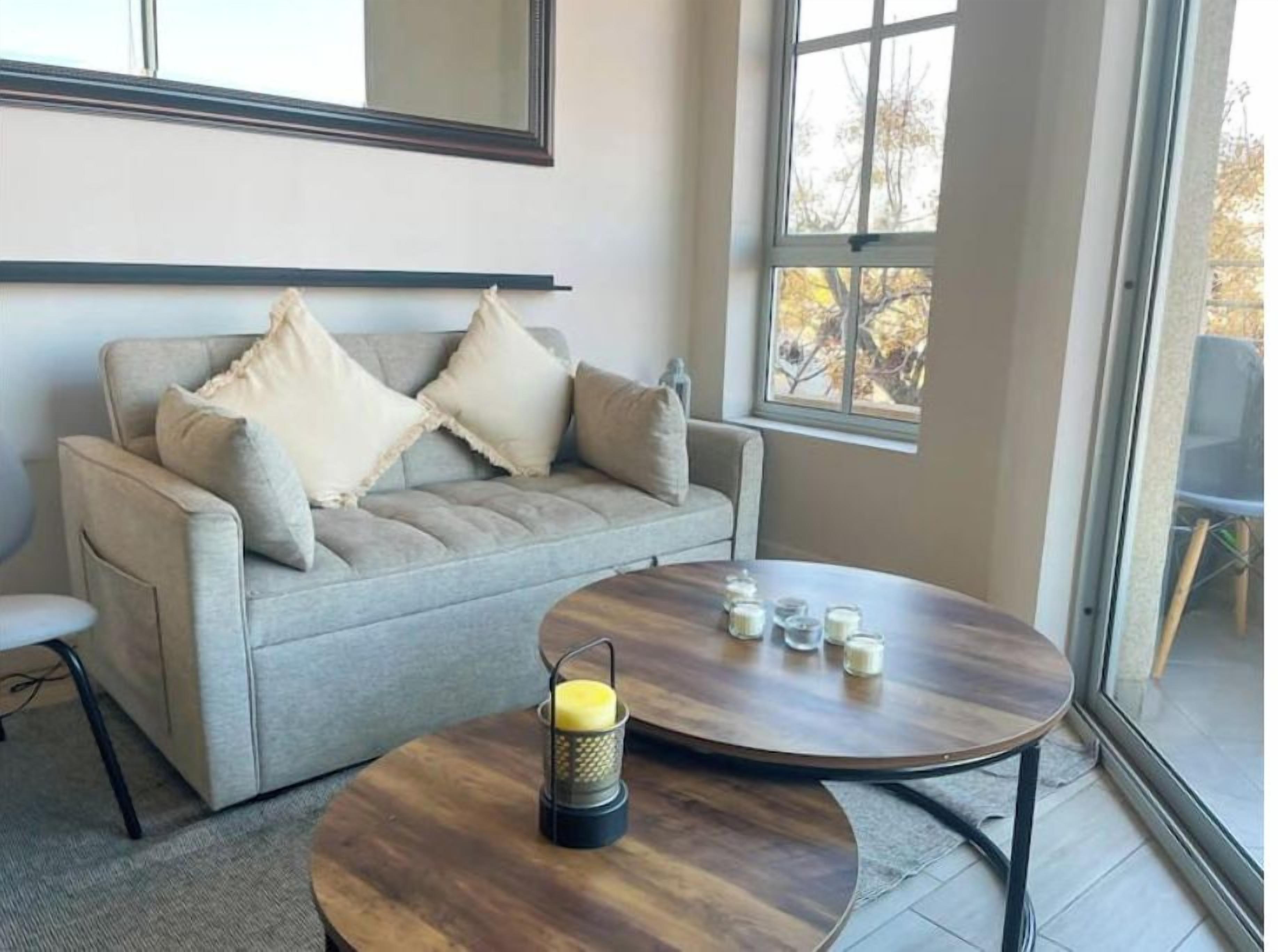 A living room with a sofa, a round wooden coffee table, and a window with a view.