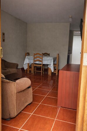 Ein Wohnzimmer mit braunem Sofa, einem Esstisch mit Stühlen und einer Küchenzeile mit roter Arbeitsplatte.