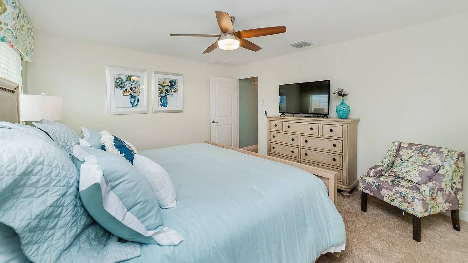 A bedroom with a bed, dresser, television, and a chair.
