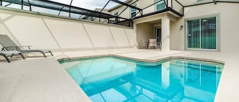 Una piscina con fondo de cristal, rodeada por un porche cubierto con sillas.