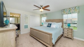 Ein Schlafzimmer mit Bett, Deckenventilator, Nachttisch, Kommode und Fenster mit Jalousien.