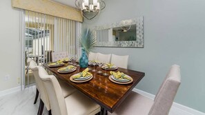 En matplats med ett träbord för fyra personer, vita stoppade stolar, en stor spegel och en takfläkt.