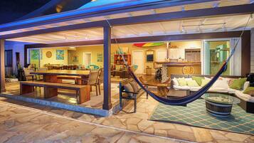 A covered outdoor area with a dining table, chairs, a hammock, and a kitchen area.