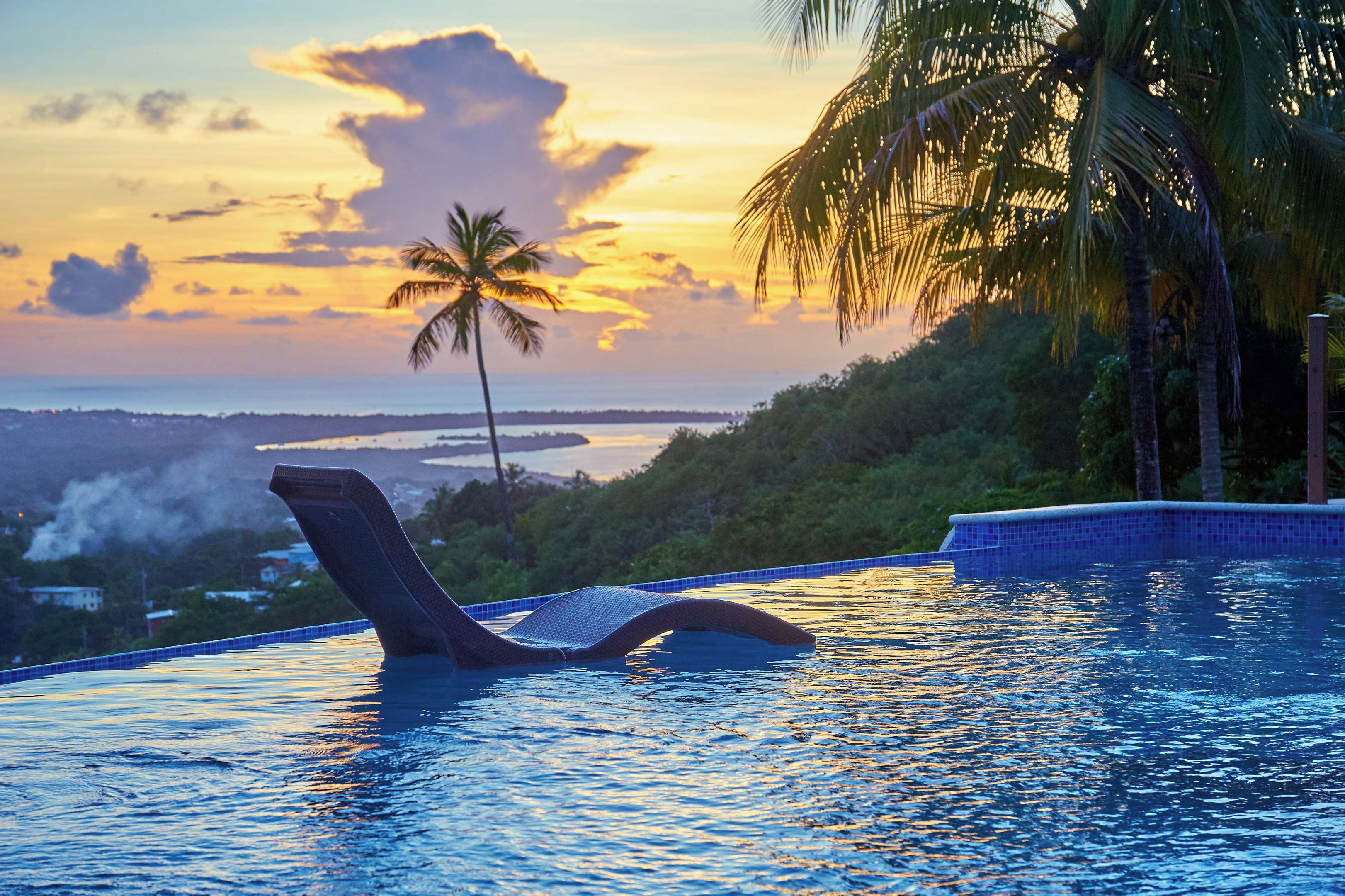 Una piscina con una silla de descanso, palmeras y vistas al atardecer.