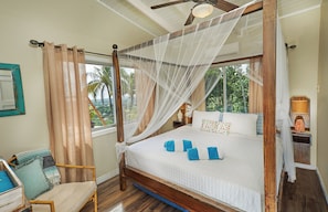 A four-poster bed with a canopy, a wooden chair, and a nightstand with a lamp.